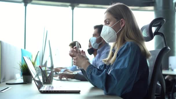Młoda kobieta biznesu nosząca maskę do twarzy czyszcząca ręce żelem dezynfekującym w miejscu pracy — Wideo stockowe