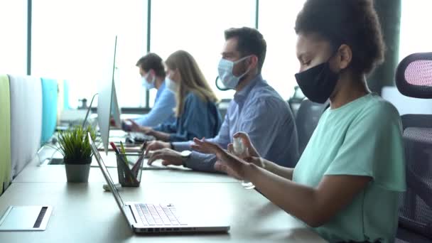 Молода змішана гонка бізнес-леді в масці для очищення обличчя з гелем для дезінфекції на робочому місці — стокове відео