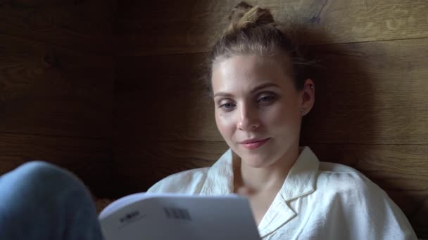 Красивая женщина лежит на диване, читает журналы в свободное время, и отдыхает по утрам — стоковое видео