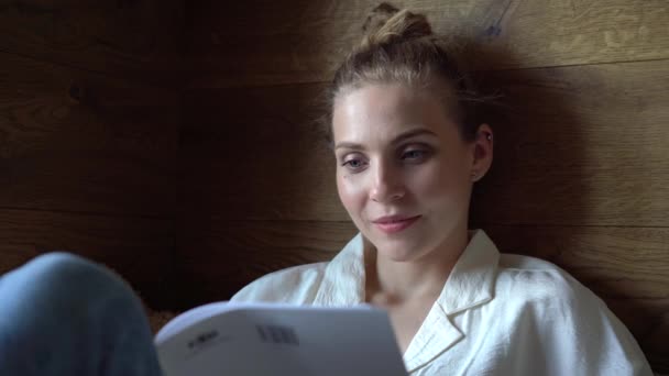 Piękna kobieta leży na kanapie, czyta czasopisma w wolnym czasie i relaksuje się rano — Wideo stockowe