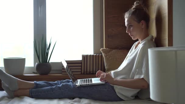 Młoda szczęśliwa kobieta relaksująca się na kanapie, korzystająca z komputera w domu, pisząca wiadomość, komunikująca się ze znajomymi lub robiąca zakupy — Wideo stockowe