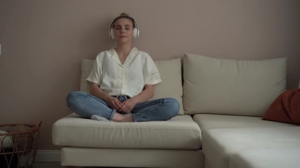 Tenang wanita muda dingin di sofa dengan mata tertutup mengenakan headphone — Stok Video