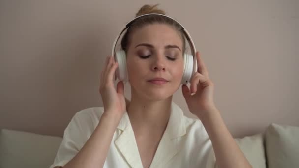 Calma relajada mujer joven que se enfría en el sofá con los ojos cerrados usando auriculares — Vídeos de Stock