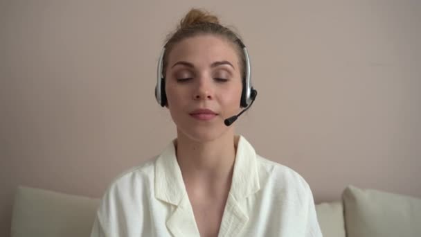 Mutlu genç bir kadın web kamerasına kulaklık takıyor ve uzaktan video konferans görüşmesi yapıyor. — Stok video