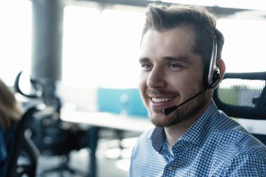 Çağrı merkezinde çalışan, kulaklık takan genç, yakışıklı bir erkek müşteri destek operatörü.