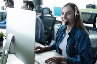 Size nasıl yardımcı olabilirim? Kulaklıklı güzel çağrı merkezi çalışanları modern ofiste çalışıyor.