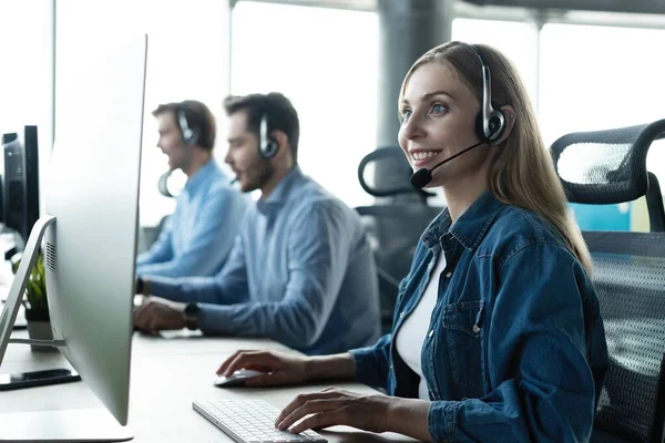 Como posso ajudá-lo? Belos trabalhadores de call center em fones de ouvido estão trabalhando no escritório moderno — Fotografia de Stock