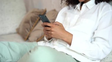 Mutlu, genç, melez bir kadın. Kanepede dinleniyor, akıllı telefon kullanıyor, mesaj yazıyor.
