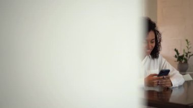 Neşeli, genç, melez bir kadın sohbet ediyor. İş sırasında akıllı telefon kullanıyor, eğleniyor.