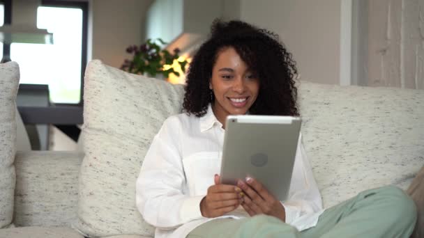 Mixed race woman sit on sofa talk by videocall app on tablet, communicating — Stock Video