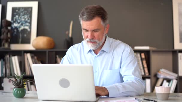 Een serieuze volwassen man werkt met zijn laptop computer op kantoor. — Stockvideo