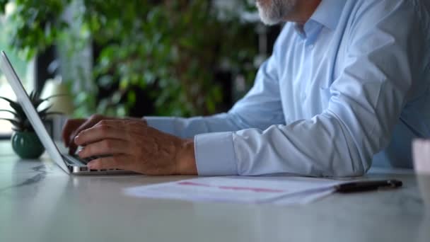 Een serieuze volwassen man werkt met zijn laptop computer op kantoor. — Stockvideo