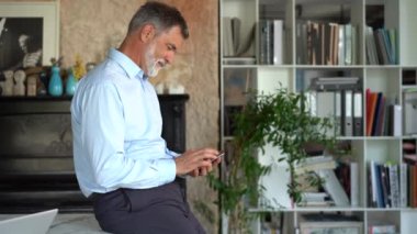 Ofiste elinde akıllı telefonla gülümseyen olgun iş adamı. 60 'ların yöneticisi cep telefonu uygulamaları kullanıyor.