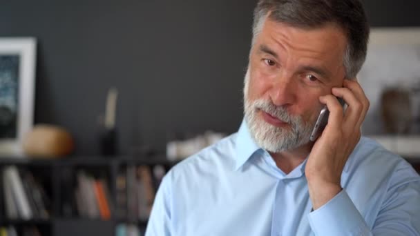 Een glimlachende, volwassen zakenman die een smartphone in zijn kantoor houdt. 60-jarige manager ceo met behulp van mobiele telefoon mobiele apps. — Stockvideo