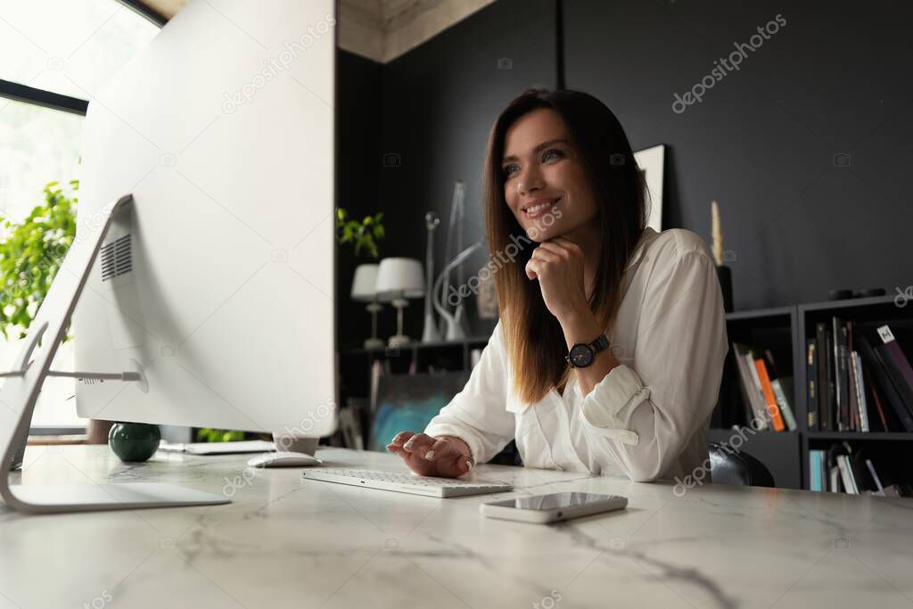 Attractive young woman working at office, using contemporary desktop computer.