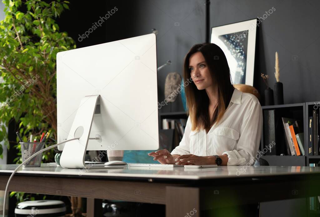 Attractive young woman working at office, using contemporary desktop computer.