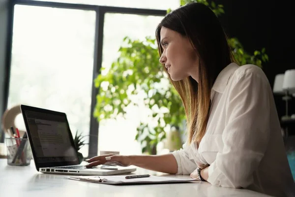 Красива жінка аналітик даних сидить за столом працює на ноутбуці. Стильна жінка в сучасному офісному середовищі . — стокове фото