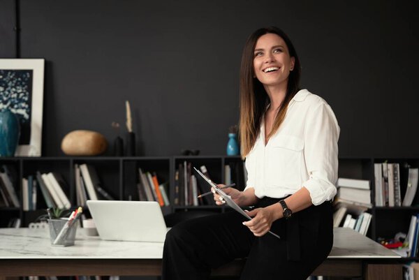 Confident stylish european middle aged woman standing at workplace, 30s lady executive leader manager looking at camera