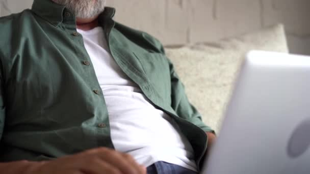 Starší starší starší muž psaní na notebooku procházení internetu pomocí aplikací sedí na pohovce sám — Stock video