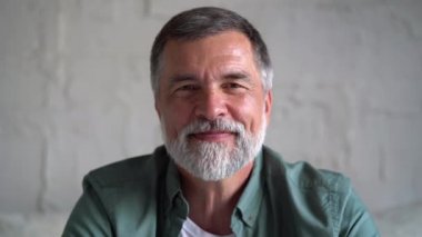 Kanepede dinlenen gülümseyen olgun bir adam. Gri saçlı, evde dinlenen ve kameraya bakan kendinden emin son sınıf öğrencisi.