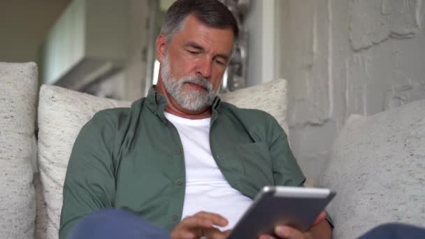 Uśmiechnięty siwowłosy dojrzały mężczyzna websurfing w Internecie z tabletem — Wideo stockowe