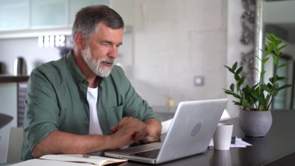 Der bärtige Mann arbeitet online mit dem Laptop zu Hause am Schreibtisch. Home Office, Surfen im Internet. — Stockvideo