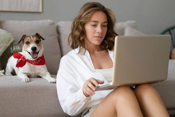 Beautiful young woman with cute dog working on laptop at home. — Stock Photo, Image