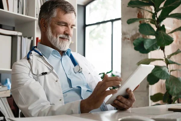 Vidám érett orvos segítségével digitális tabletta a klinikán. — Stock Fotó