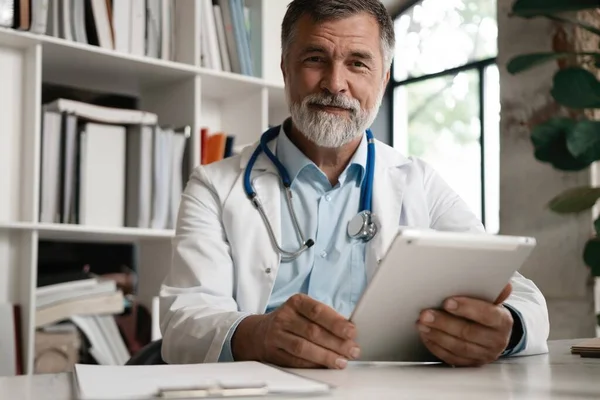 Radosny dojrzały lekarz korzystający z tabletu cyfrowego w klinice. — Zdjęcie stockowe