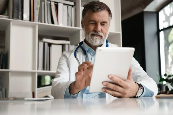 Radosny dojrzały lekarz korzystający z tabletu cyfrowego w klinice. — Zdjęcie stockowe