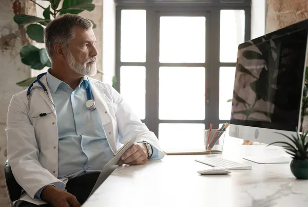 Portrait of handsome doctor sitting at desk, taking notes or fills in the clients medical card or prescribes medication