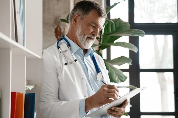 Retrato de guapo médico maduro de pie en la ventana en la oficina moderna. — Foto de Stock