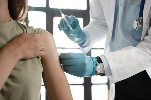 Closeup of a nervous woman and her doctor wearing face masks and getting a vaccine shot in a doctors office.