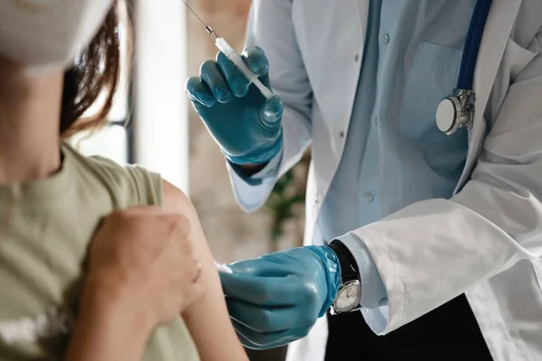 Closeup of a nervous woman and her doctor wearing face masks and getting a vaccine shot in a doctors office.