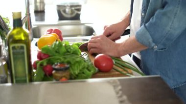 Genç ve mutlu bir adam evde tek başına sağlıklı yiyecekler hazırlıyor. Modern mutfak içinde taze sebze salatası kesiyor.