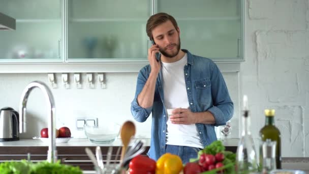 Vit man som använder smartphone och pratar i köket hemma — Stockvideo