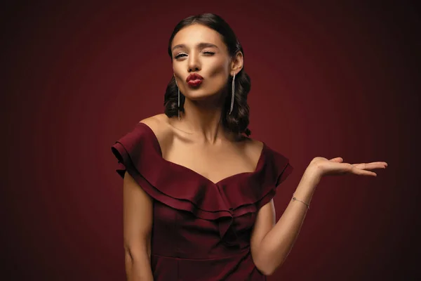 Menina modelo bonita com penteado elegante em vestido vermelho mostrando produto. Menina bonita apontando para o lado — Fotografia de Stock