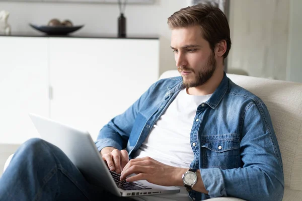 Un bell'uomo che usa il computer portatile a casa. Shopping online, lavoro a casa, freelance, apprendimento online, concetto di studio — Foto Stock