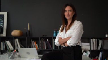 Kendinden emin gülümseyen genç Avrupalı kadın ofiste duran kameraya bakıyor, kapalı alanda portre için poz veriyor.