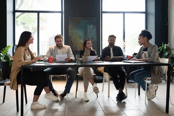 Felices compañeros de trabajo trabajando juntos discutiendo el proyecto sentado en un escritorio en la oficina moderna. Panorama — Foto de Stock