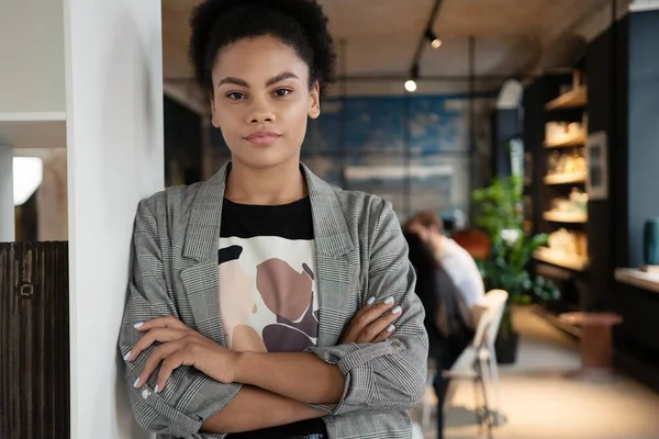 Exitosa mujer de negocios de raza mixta sonriente de pie en la oficina creativa y mirando a la cámara en la oficina moderna — Foto de Stock