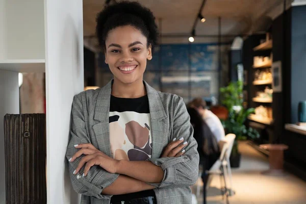 Successful smiling mixed-race businesswoman standing in creative office and looking at camera at modern office