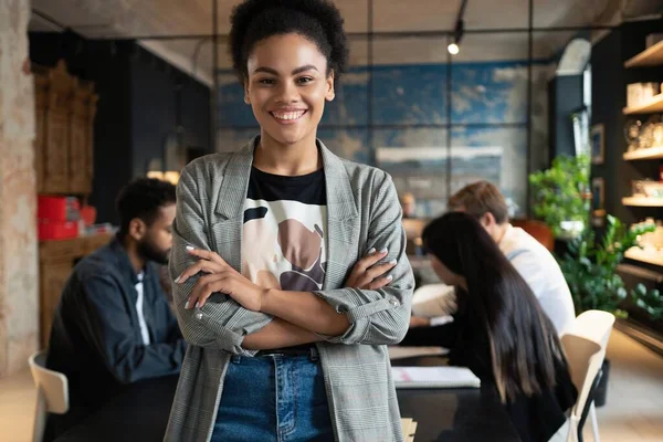 Exitosa mujer de negocios de raza mixta sonriente de pie en la oficina creativa y mirando a la cámara en la oficina moderna — Foto de Stock