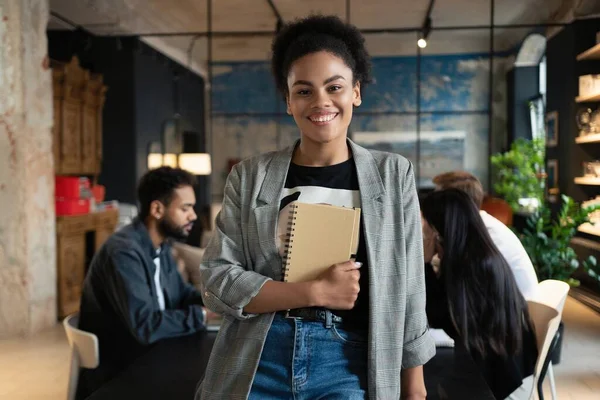 Exitosa mujer de negocios de raza mixta sonriente de pie en la oficina creativa y mirando a la cámara en la oficina moderna — Foto de Stock