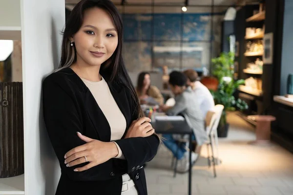 Bem sucedido sorrindo asiático empresária de pé no criativo escritório e olhando para câmera no moderno escritório Fotografias De Stock Royalty-Free