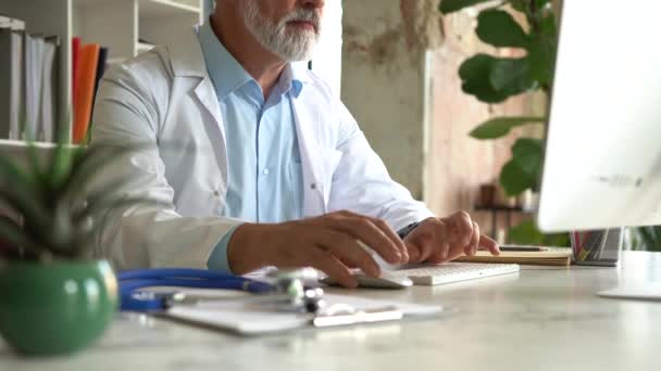 Specjalista medyczny w mundurze pracuje z komputerowym pisaniem siedząc przy biurku w gabinecie kliniki — Wideo stockowe