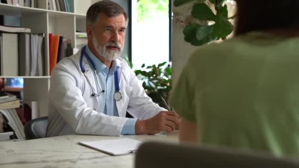 Ernsthaft fokussierter gealterter Arzt im Arztkittel sitzt am Tisch und berät Patientin über Krankheit oder Operation — Stockvideo