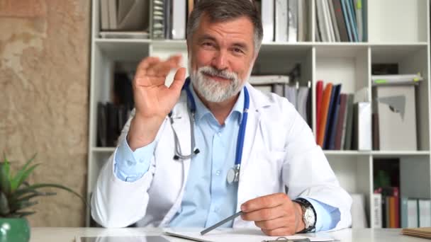 Beyaz üniformalı profesyonel erkek doktor kameraya bakıyor uzaktan hastayla konuşuyor, webcam görüntüsü var. — Stok video