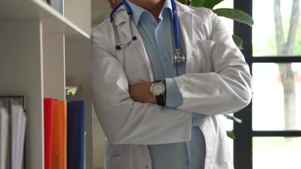 웃고 있는 장성 한 전문의 가 병원 사무실에 서 있는 카메라를 보면서 흰색의 의료 복을 입고 있다 — 비디오