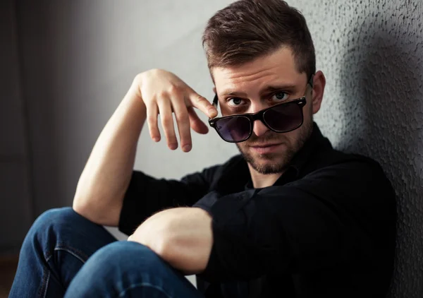 Fashion young man holding his fashionable sunglasses on gray — Stock Photo, Image